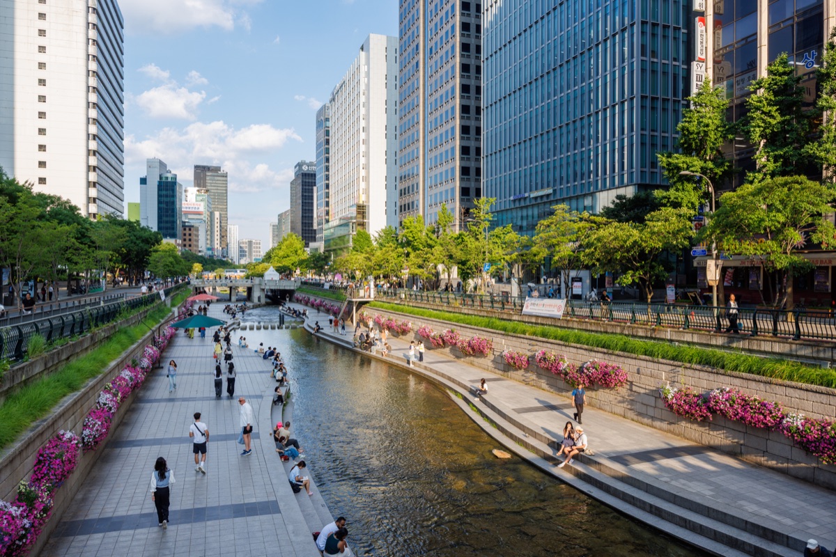 Visitors walk along Cheonggyecheon Stream surrounded by modern office towers in downtown Seoul
