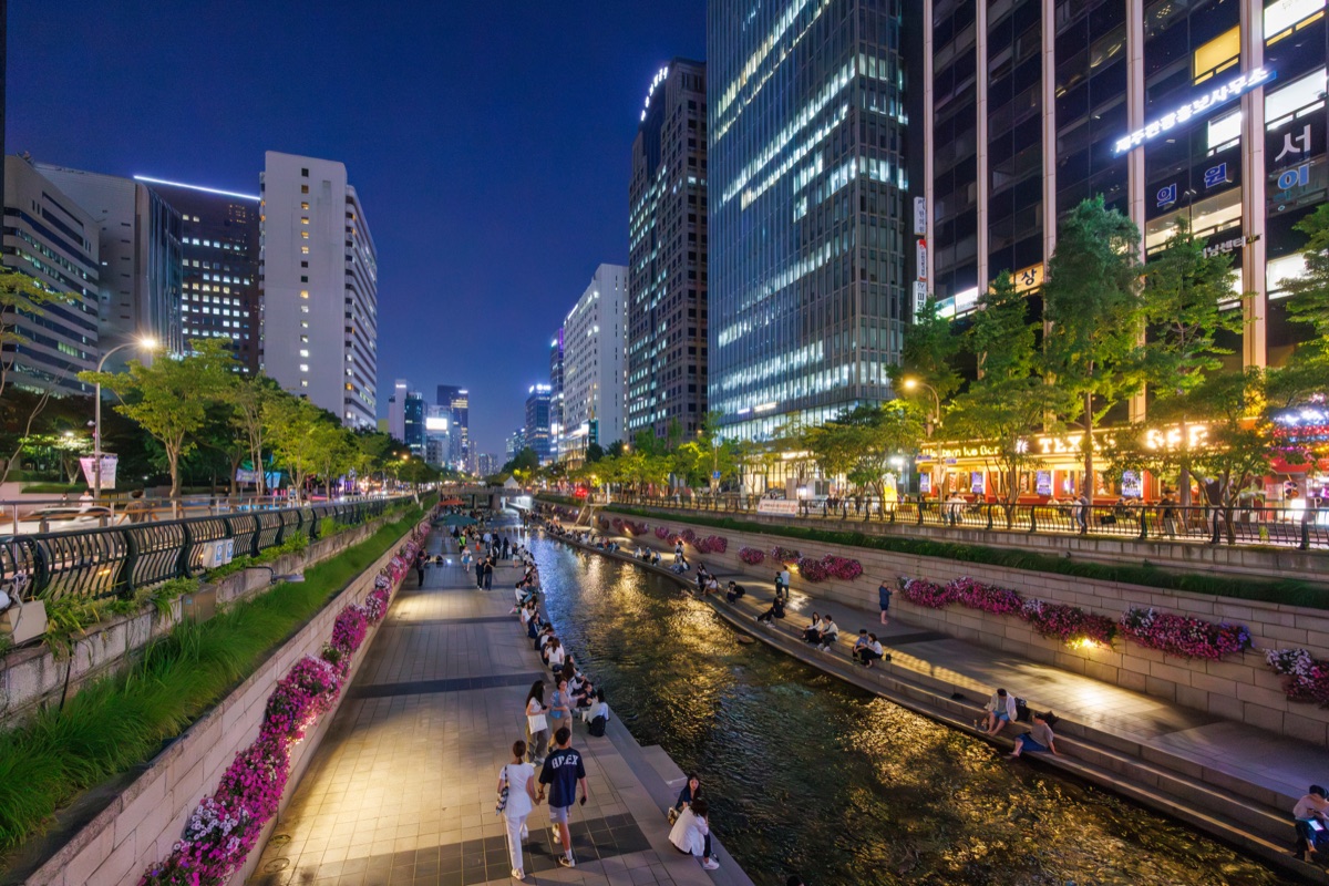 Visitors relax along Cheonggyecheon Stream surrounded by illuminated office buildings in central Seoul