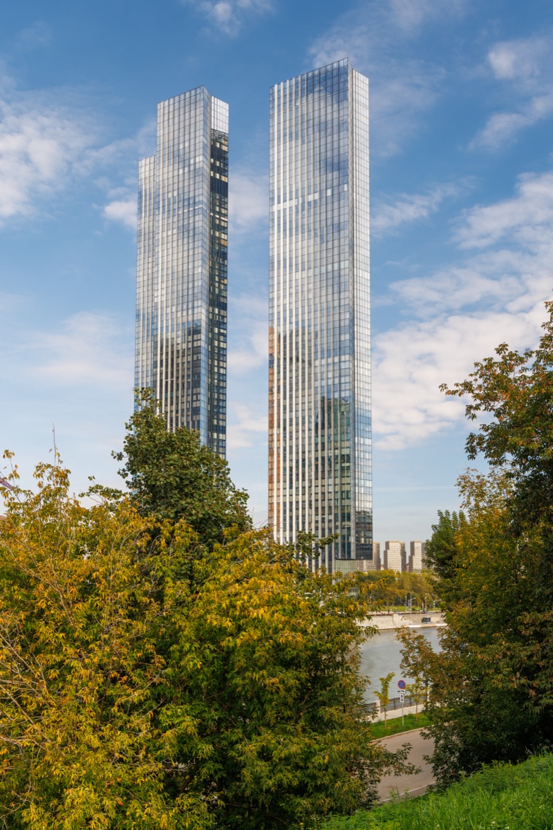 Slender Capital Towers skyscrapers appear between leafy branches above trees along the Moskva River.
