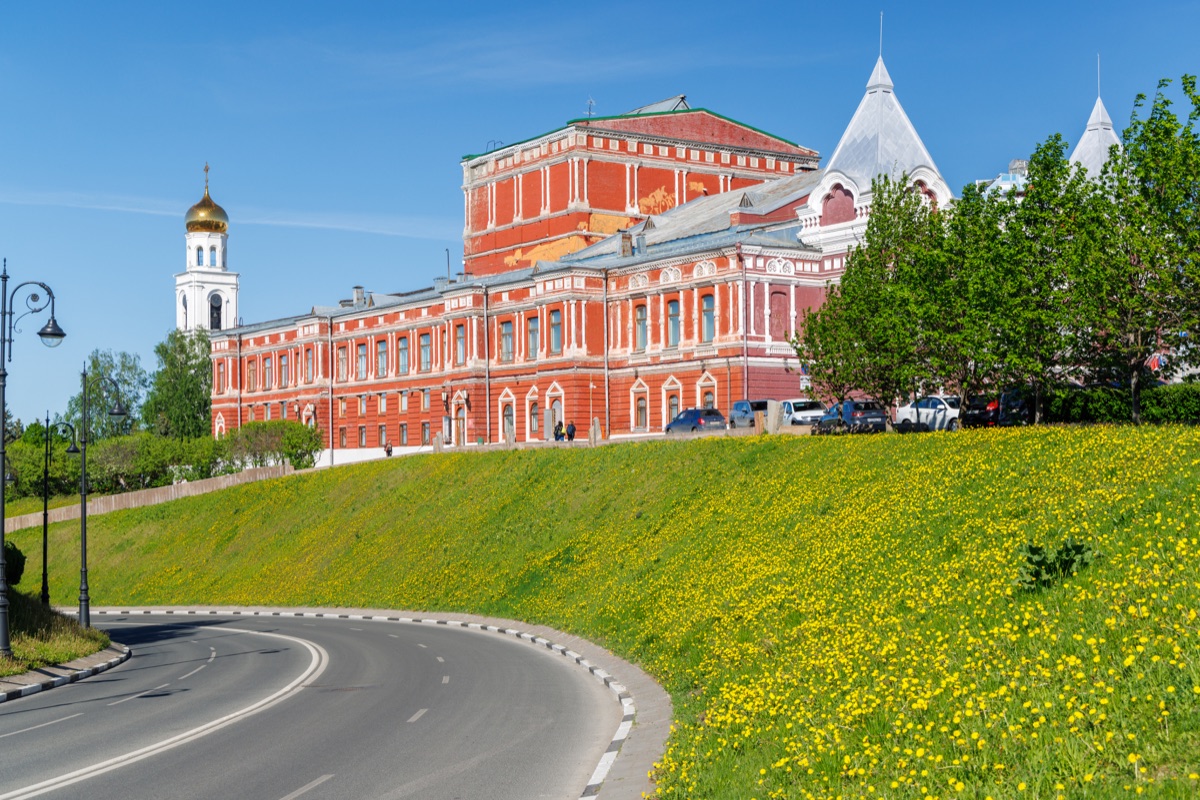 Samara Drama Theater building above green spring hill with yellow flowers on sunny day
