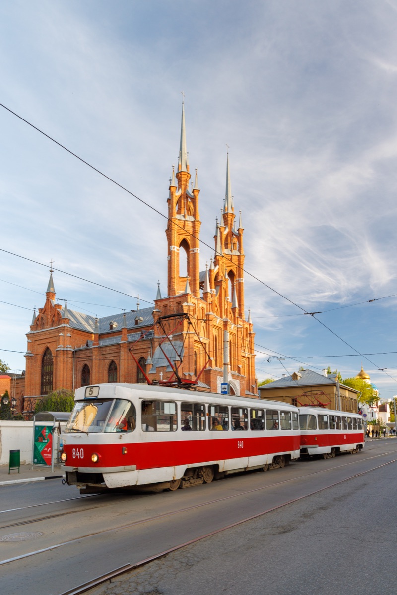 Vintage red and white tram passing historic gothic church in Samara during golden hour