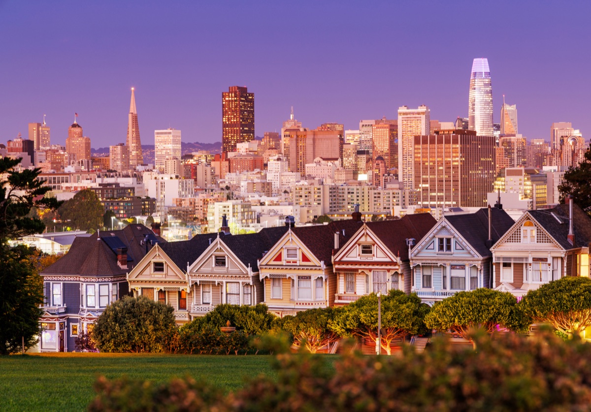 Vibrant sunset view of the Painted Ladies in San Francisco, iconic Victorian houses glowing under the warm hues of a colorful sky, with the city skyline in the background