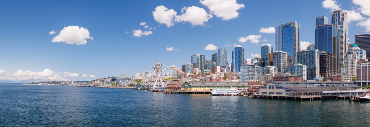 Bright and sunny panoramic view of Seattle skyline from the water, featuring the iconic Space Needle and city buildings under a clear blue sky